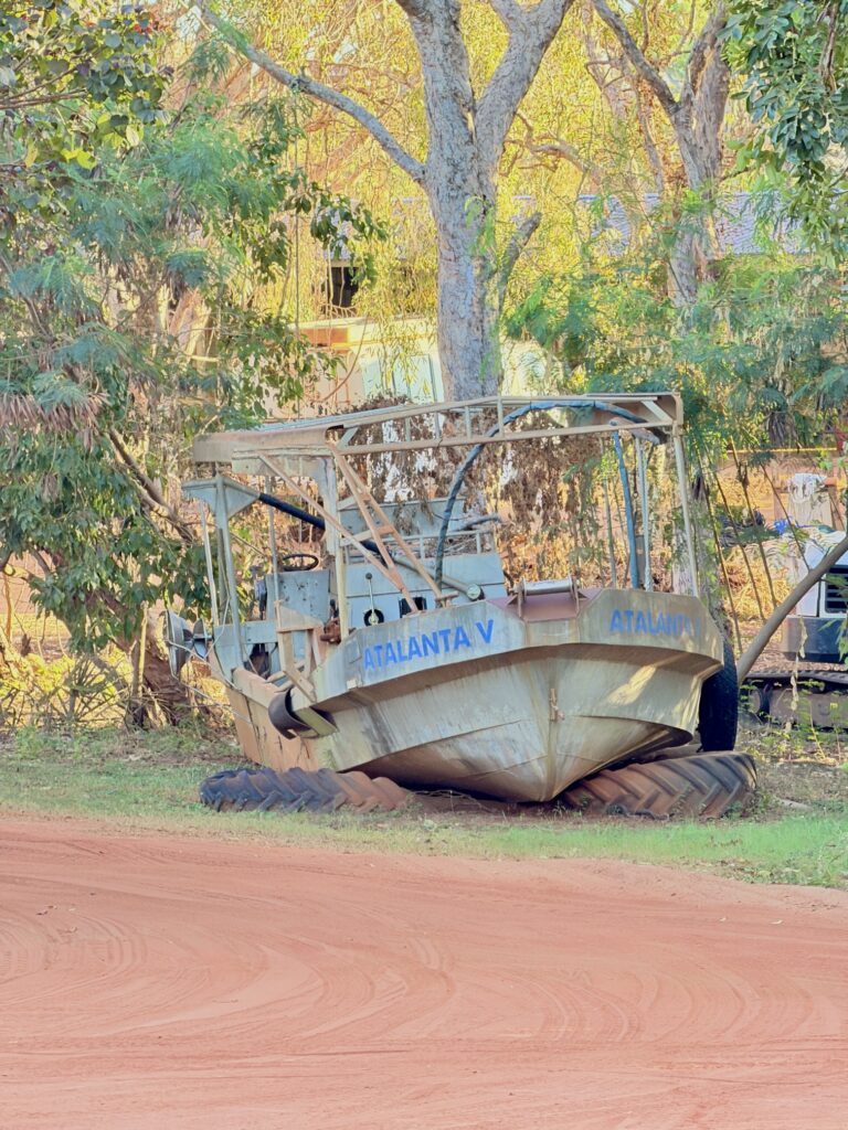 An old workboat, the Atalanta V, resting under the trees beside a red dirt road