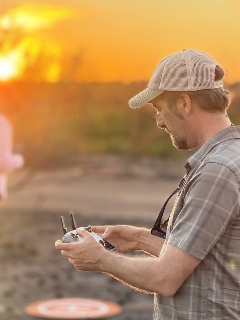 A photographer flying a drone in warm golden hour light