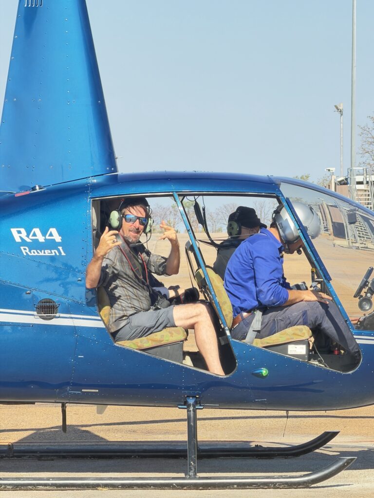 A photographer in the back of a blue R44 helicopter, ready for take-off