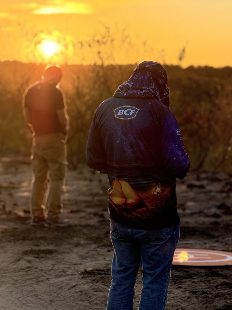 Two photographers silhouetted at sunset beside a drone landing pad