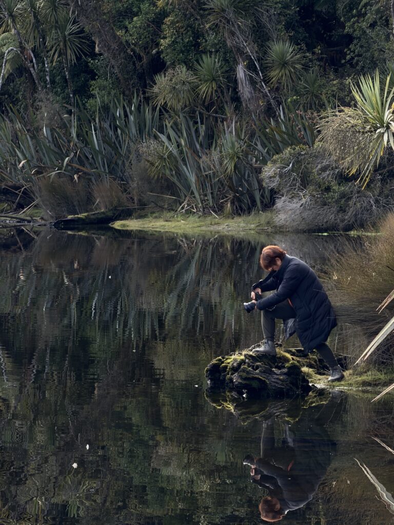 A guest crouched on a mossy rock shooting reflections in a rainforest lake